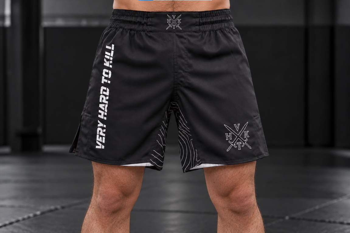 Front view of an athlete wearing VHTK Black Phantom grappling shorts with white branding and a patterned inner stretch panel.