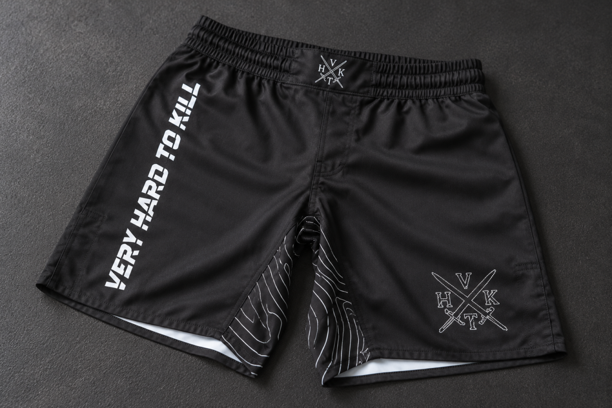 VHTK Black Phantom grappling shorts laid on a charcoal mat, showing white branding and a patterned inner thigh panel.