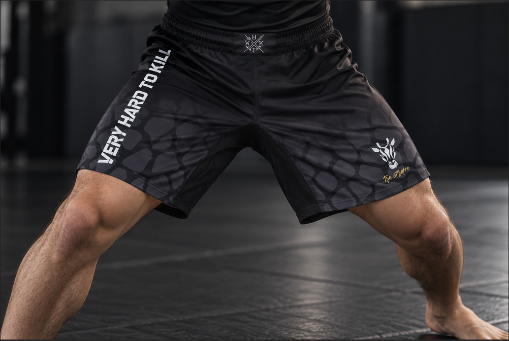 Athlete wearing VHTK All Black Giraffe shorts in a wide grappling stance, showing the black inner thigh panel and giraffe artwork.