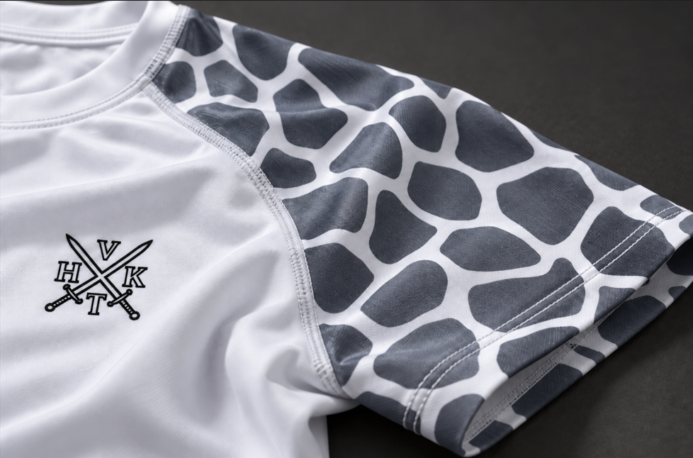 Close-up of VHTK All White Giraffe rash guard showing grey sleeve patterns, panel stitching and black chest branding.