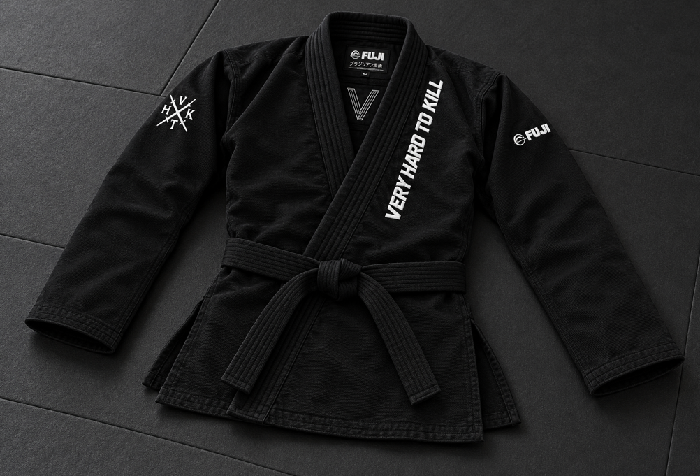 Black VHTK X FUJI BJJ gi jacket laid on a training mat, showing the tied belt, long sleeves and side openings.