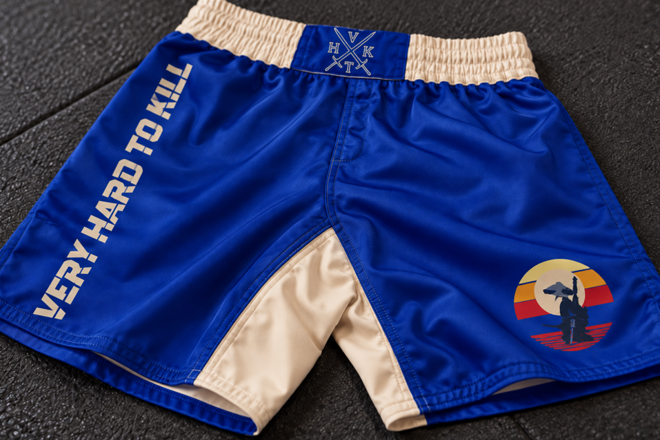 Close-up of VHTK Blue Samurai grappling shorts on a dark mat, showing stitching around the cream inner thigh panel and leg hems.