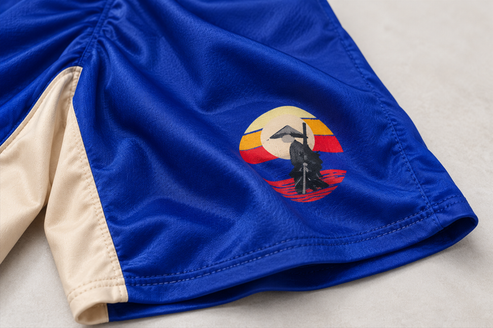 Close-up of the Samurai graphic on VHTK Blue Samurai shorts, showing blue fabric folds, a cream inner panel and the stitched hem.