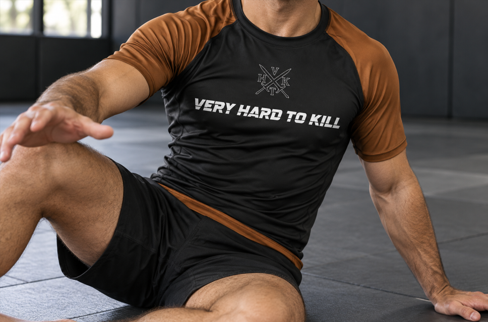 Grappler wearing VHTK Brown Rankings Edition rash guard in a seated guard position.