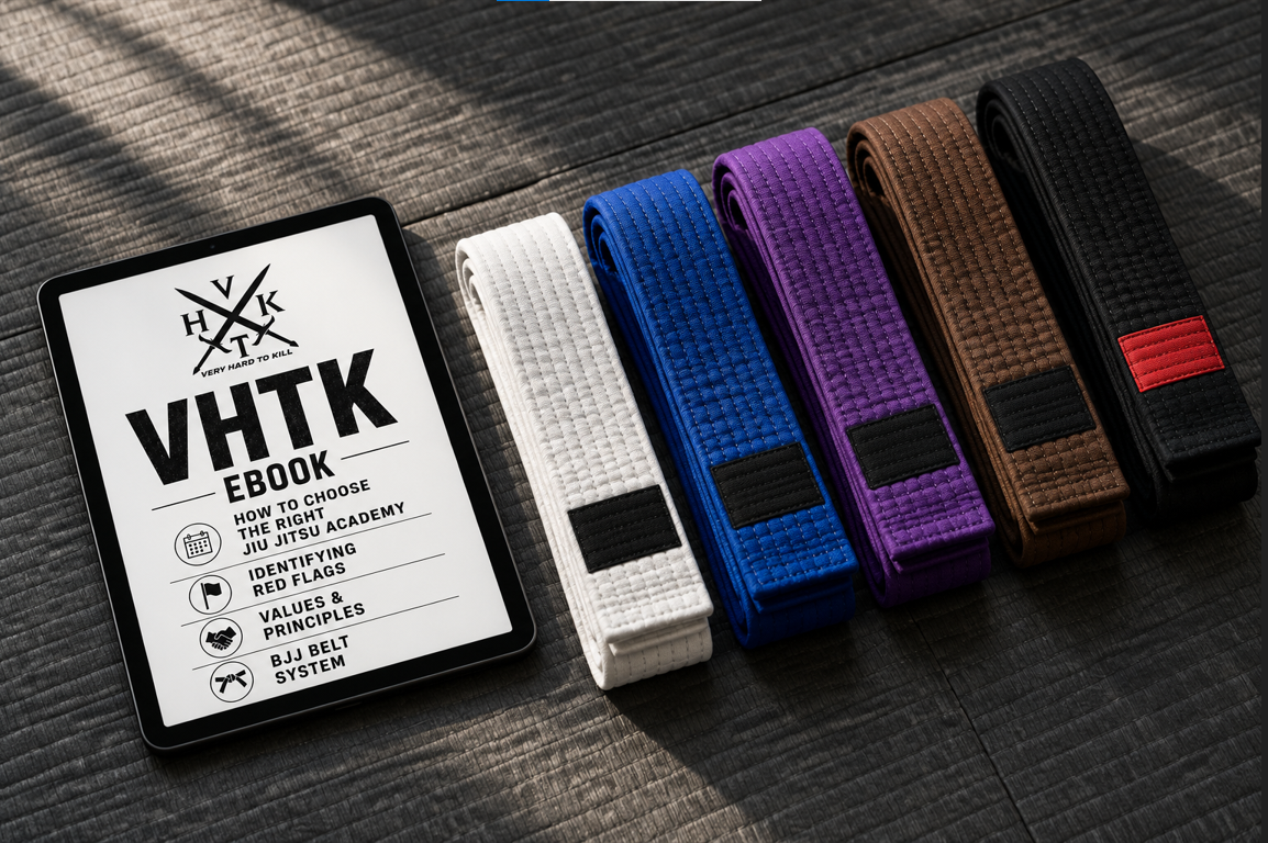 VHTK BJJ gym guide displayed on a tablet beside white, blue, purple, brown and black belts arranged on a training mat.
