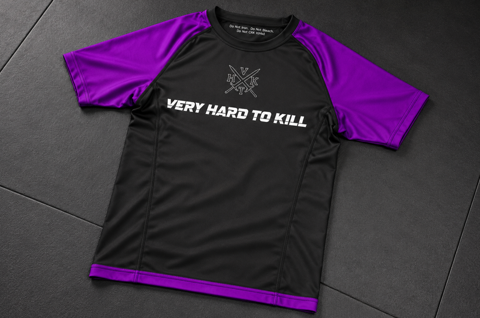 VHTK Purple Rankings rash guard laid flat on a dark BJJ mat.